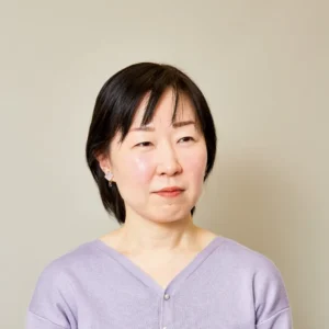 Retrato de Syou Ishida, autora japonesa, con el cabello corto y oscuro, vestida con un suéter lila y posando sobre un fondo neutro.