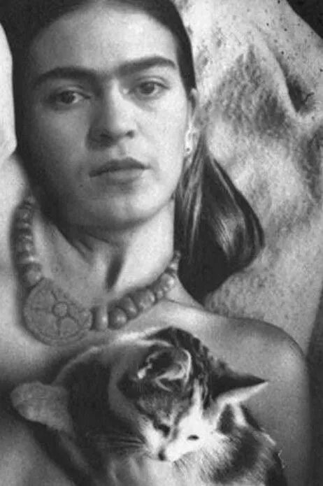 Fotografía en blanco y negro de una mujer acostada, mirando al frente, con un collar de cuentas grandes y un gato pequeño sobre el pecho.