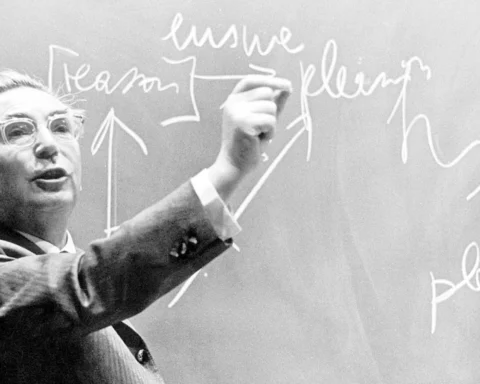 Fotografía en blanco y negro de Viktor Frankl escribiendo en una pizarra con tiza mientras gesticula durante una clase, con palabras y flechas visibles detrás de él.