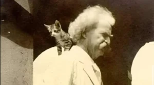 Fotografía en blanco y negro de Mark Twain con un pequeño gato apoyado sobre su hombro, mientras el escritor mira hacia un lado con gesto serio.