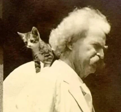 Fotografía en blanco y negro de Mark Twain con un pequeño gato apoyado sobre su hombro, mientras el escritor mira hacia un lado con gesto serio.
