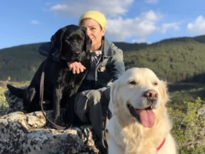 Sara Escudero sentada en un prado abrazando a un perro golden retriever entre flores silvestres.