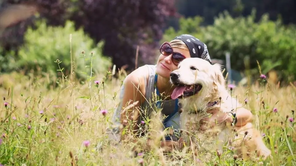 Sara Escudero posando en la naturaleza con dos perros, un labrador negro y un golden retriever, en un paisaje de montaña.