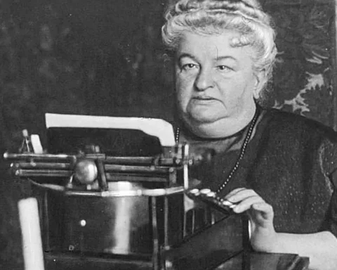 Retrato en blanco y negro de Emilia Pardo Bazán sentada ante una máquina de escribir, concentrada mientras sostiene el papel con una mano