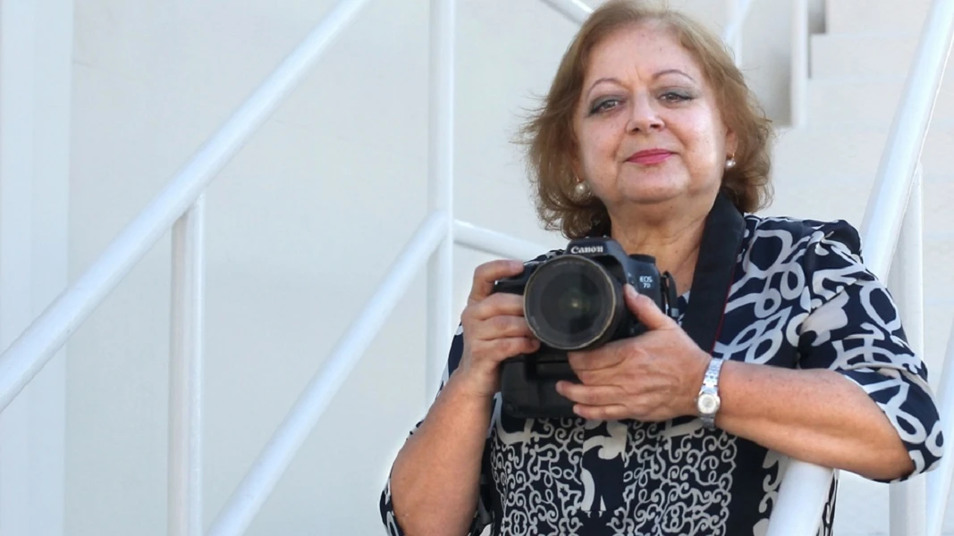 Retrato en color de Cristina García Rodero con su cámara Canon, apoyada en una escalera blanca.