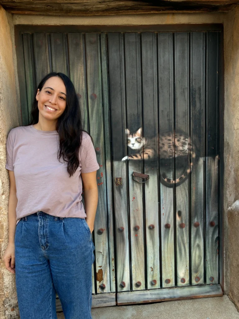Sara Ramiro sonriente apoyada junto a una puerta metálica decorada con la imagen de un gato pintado.