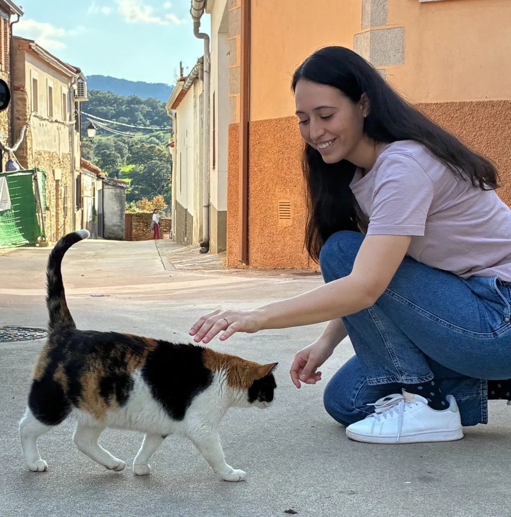 Sara Ramiro acariciando a un gato tricolor en una calle de pueblo con casas tradicionales al fondo.