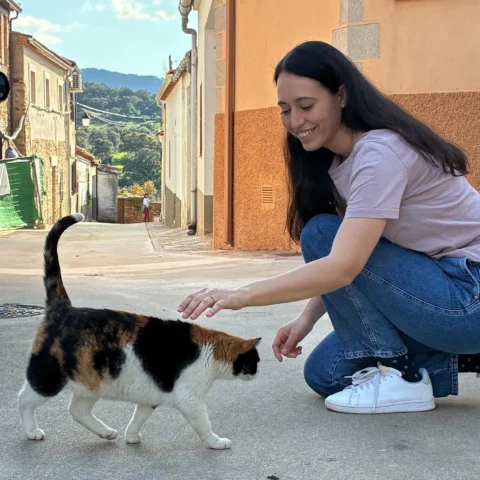 Sara Ramiro acariciando a un gato tricolor en una calle de pueblo con casas tradicionales al fondo.