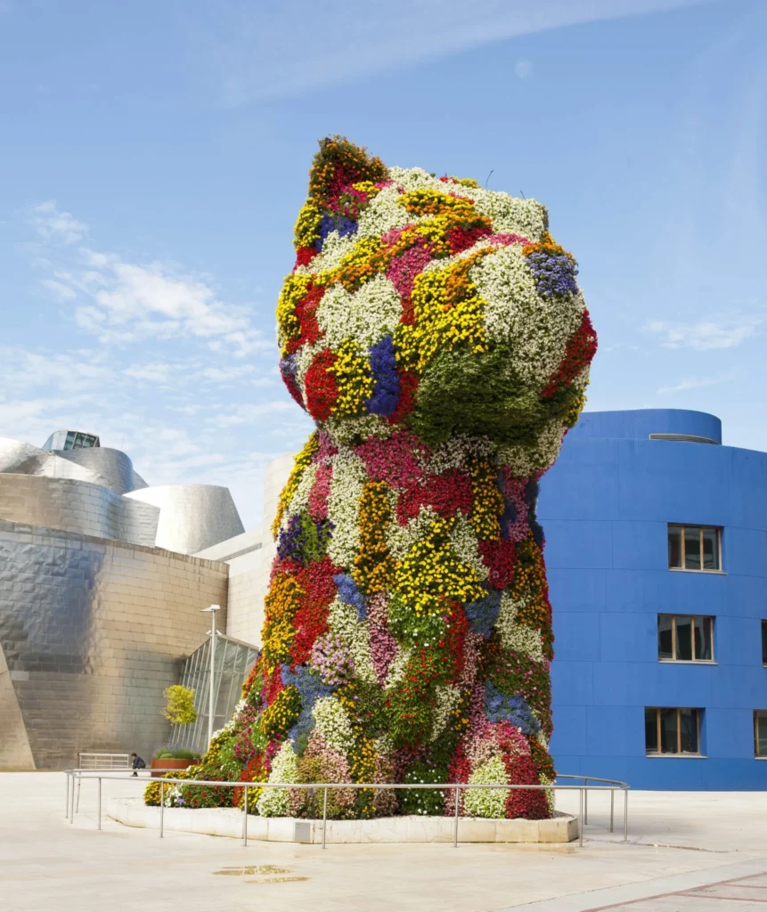 Escultura floral gigante con forma de cachorro frente al Museo Guggenheim de Bilbao bajo un cielo despejado.