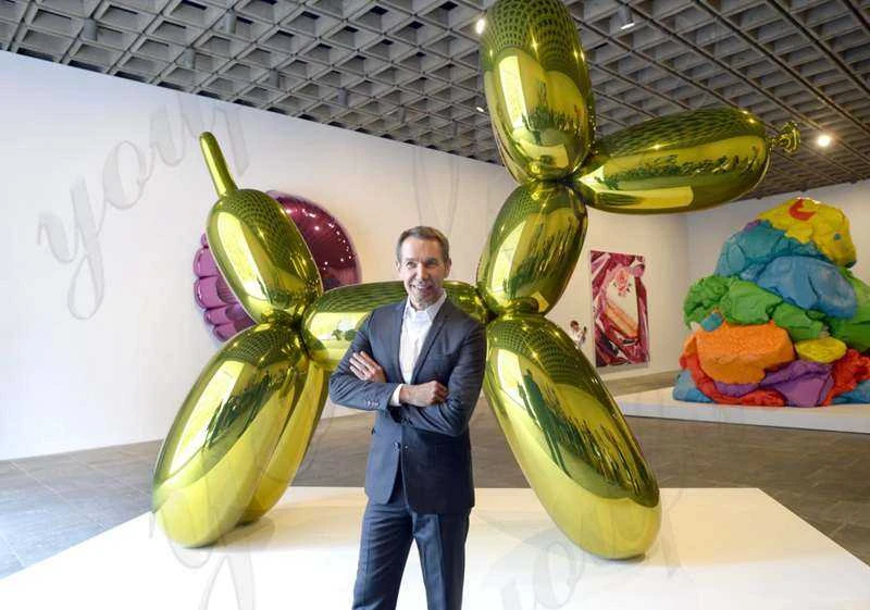 Jeff Koons de pie frente a una gran escultura verde con forma de perro globo en una exposición artística.