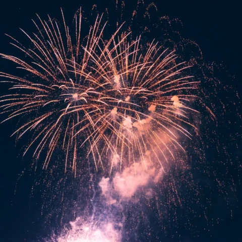 Fuegos artificiales dorados iluminando el cielo nocturno durante una celebración, con destellos brillantes y una nube de humo en la parte inferior de la explosión.